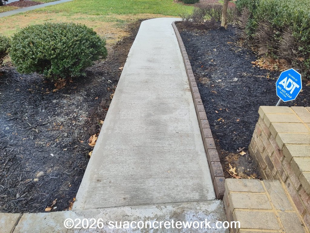 Finished concrete walkway installation along a landscaped residential property